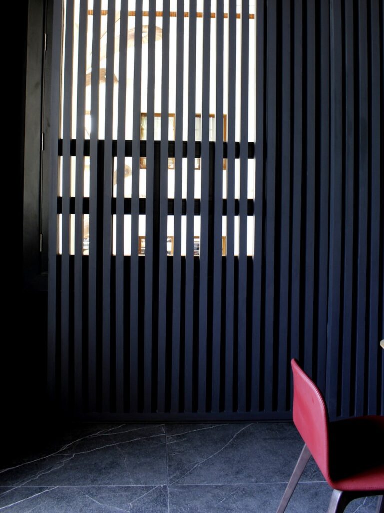 Panel de listones oscuros junto a silla roja — área de comedor