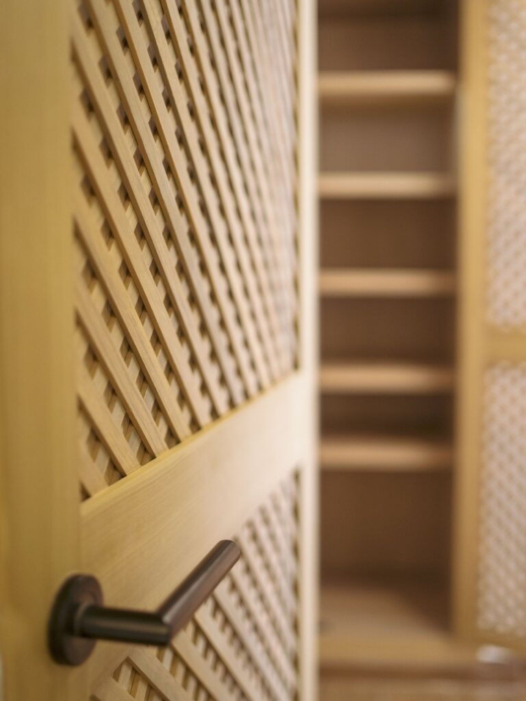 Puerta de closet de celosía entreabierta con repisas interiores de madera