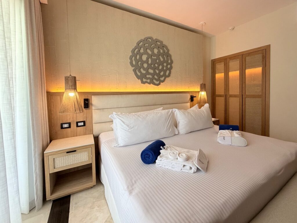 Diseño de habitación de hotel en Ocean Maya Royale con cabecera de madera, burós con rejilla y closet iluminado