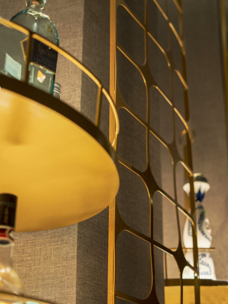 Lámpara colgante dorada junto a muro perforado y botellas decorativas