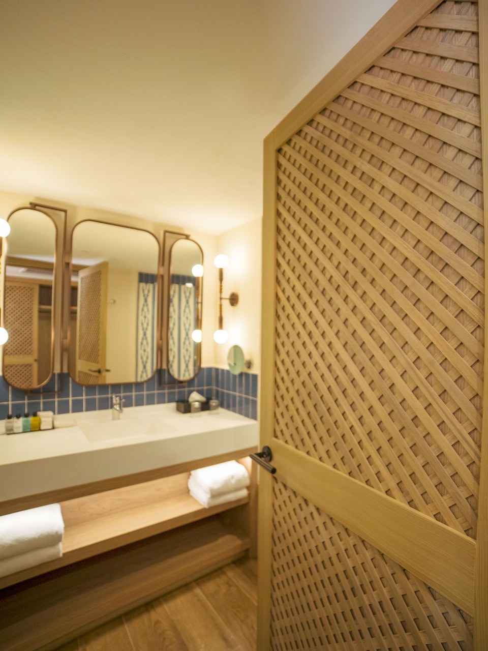 Baño de habitación en Ocean Coral & Turquesa con puerta de celosía de madera, mueble de lavabo y espejos de marco curvo
