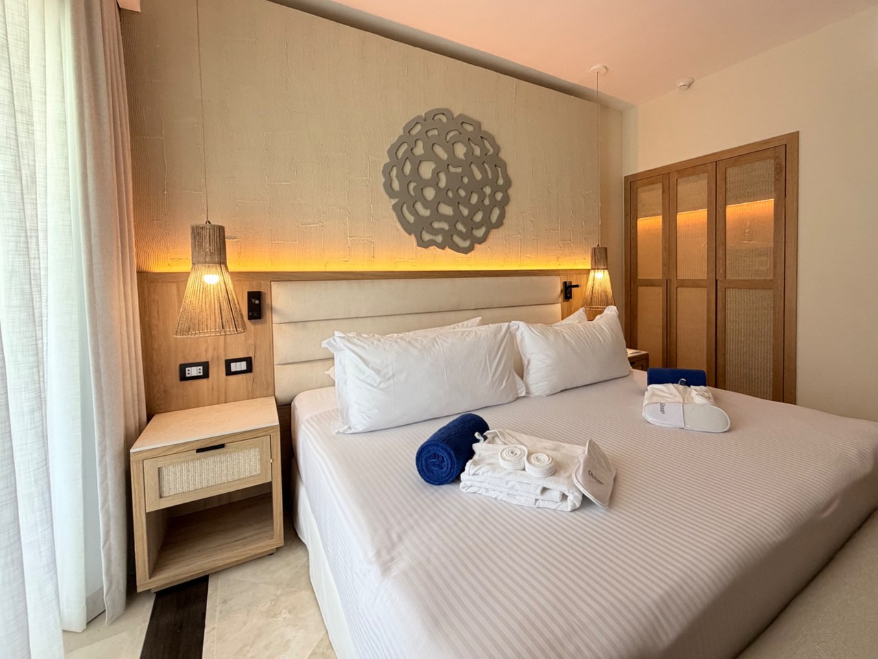 Diseño de habitación de hotel en Ocean Maya Royale con cabecera de madera, burós con rejilla y closet iluminado