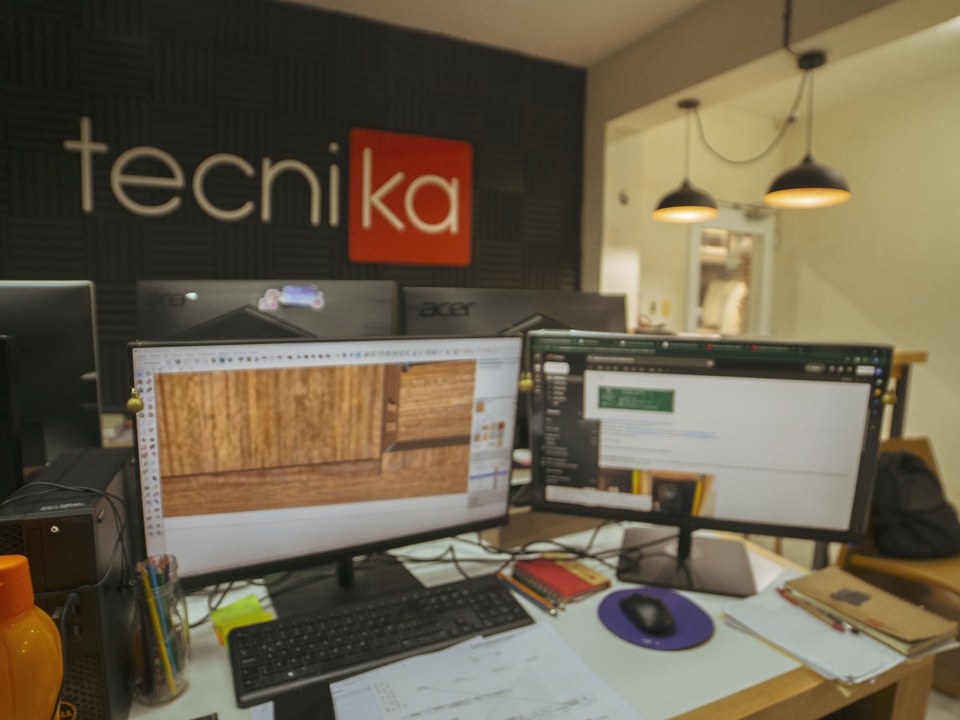 Oficina técnica de Tecnika con el logo en la pared y estaciones de trabajo con modelado 3D y planos de carpintería